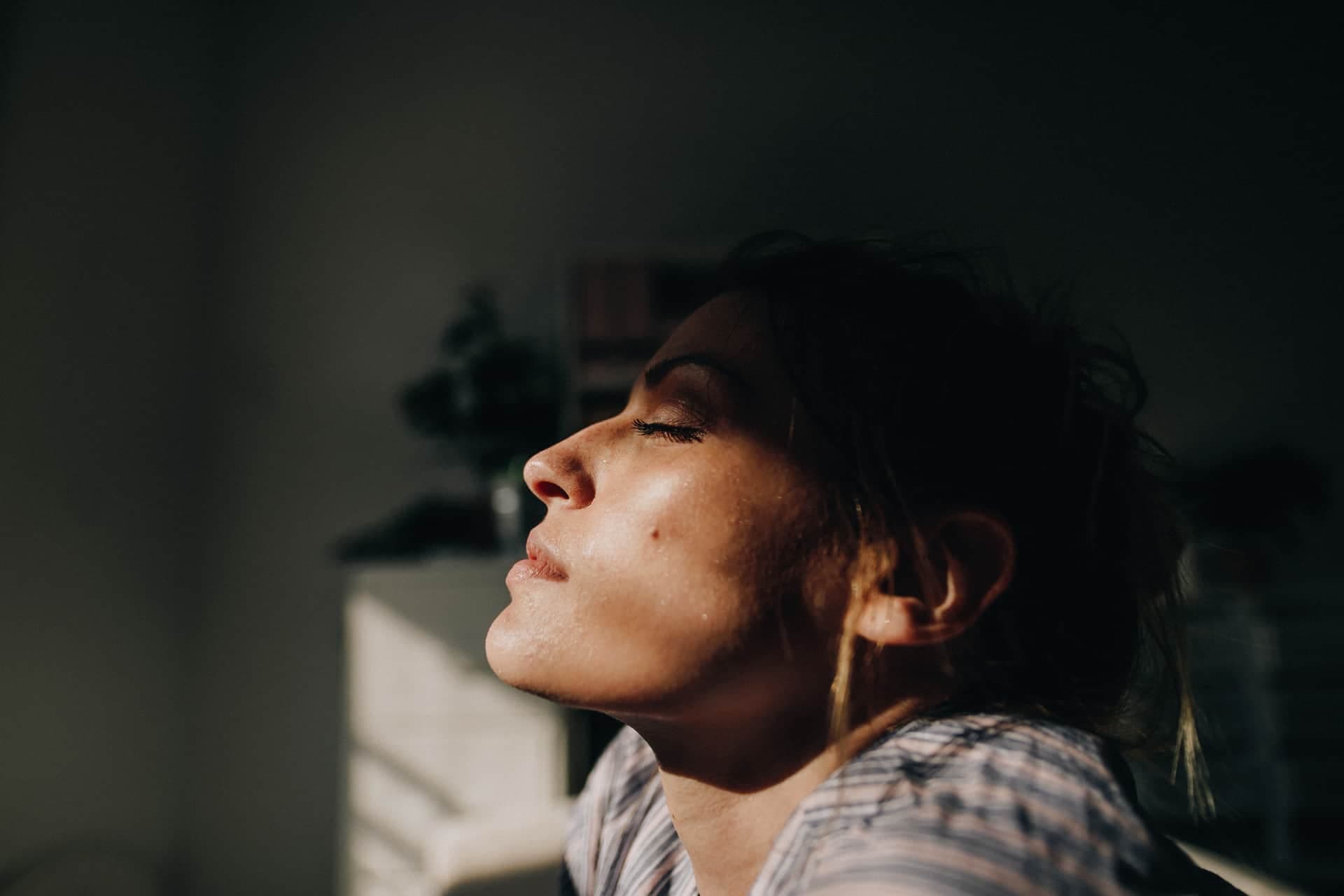 Ett porträtt i profil av en kvinna som blundar med naturligt ljus och skugga i ansiktet