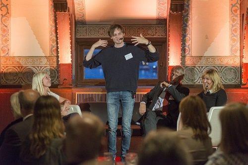 Jonas von Essen talar i en mikrofon på en scen framför publik och gestikulerar med sina händer.