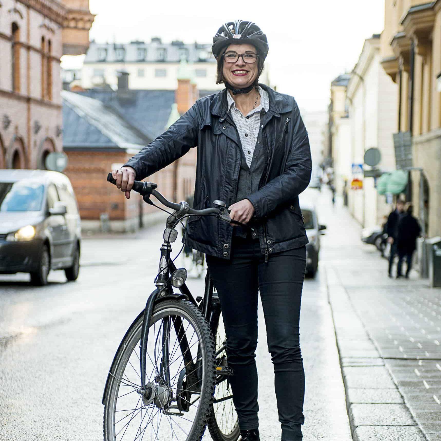 Anna Hemlin står på gatan med en el-cykel och hjälm på huvudet.