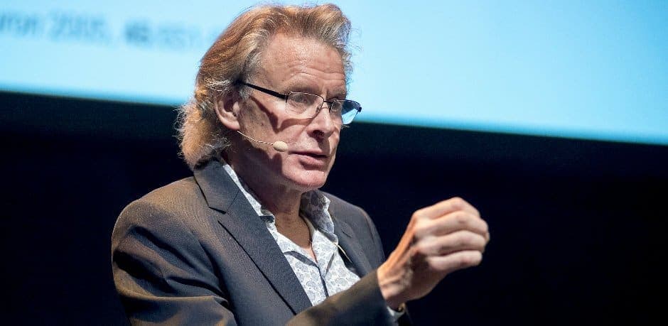 Lars Häggström talar i en mikrofon framför en stor skärm.