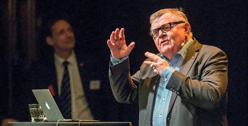 Nils Simonson talar i en mikrofon på en scen framför en laptop.