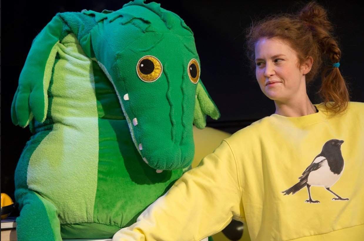 Kvinna står på scen med en stor krokodil gosedjur.