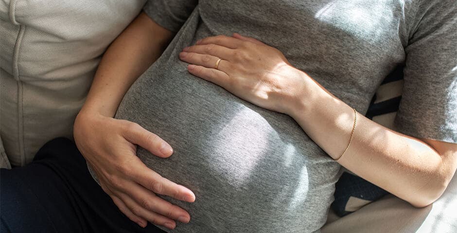 Gravid kvinna sitter och håller om sin mage