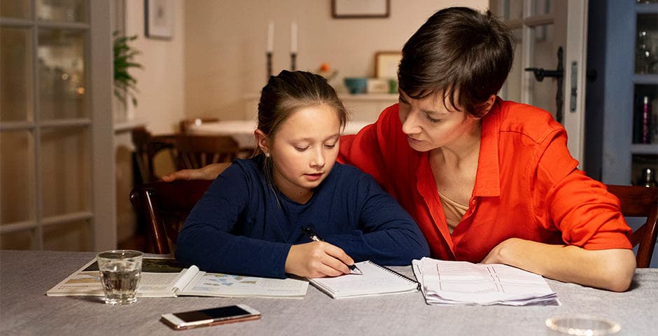 Mamma och dotter med epilepsi sitter vid köksbord och gör läxor