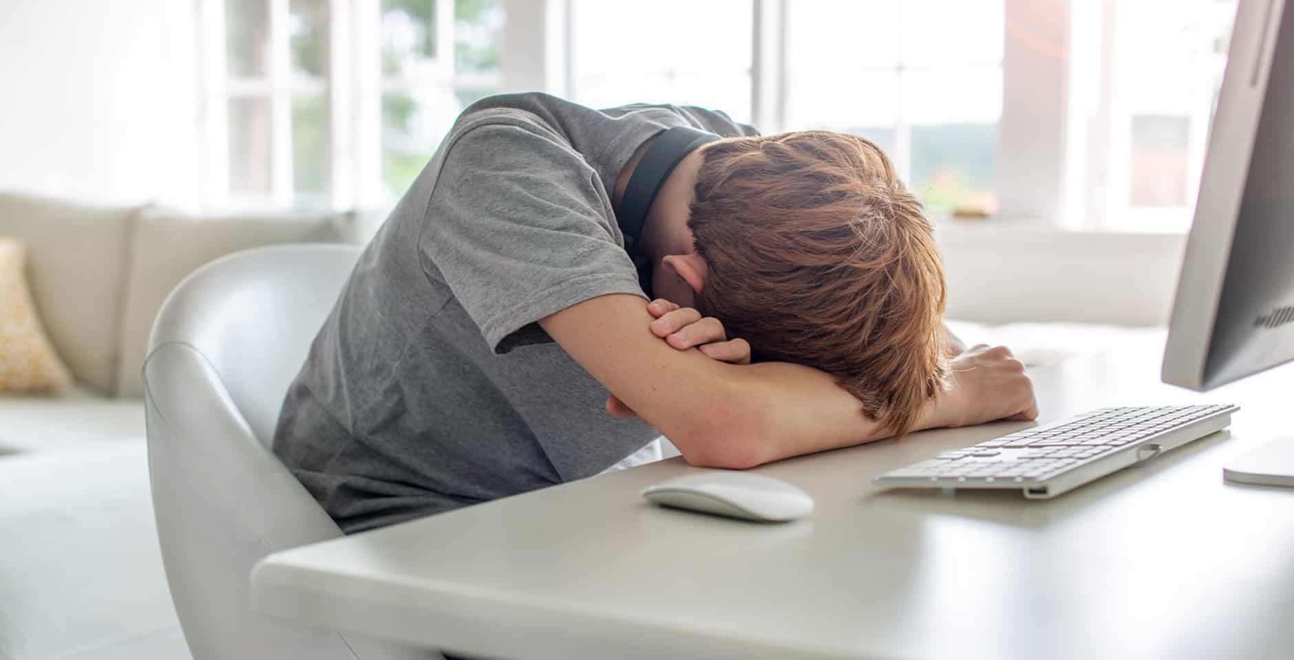 Ung kille ligger nedlutad framför sin dator