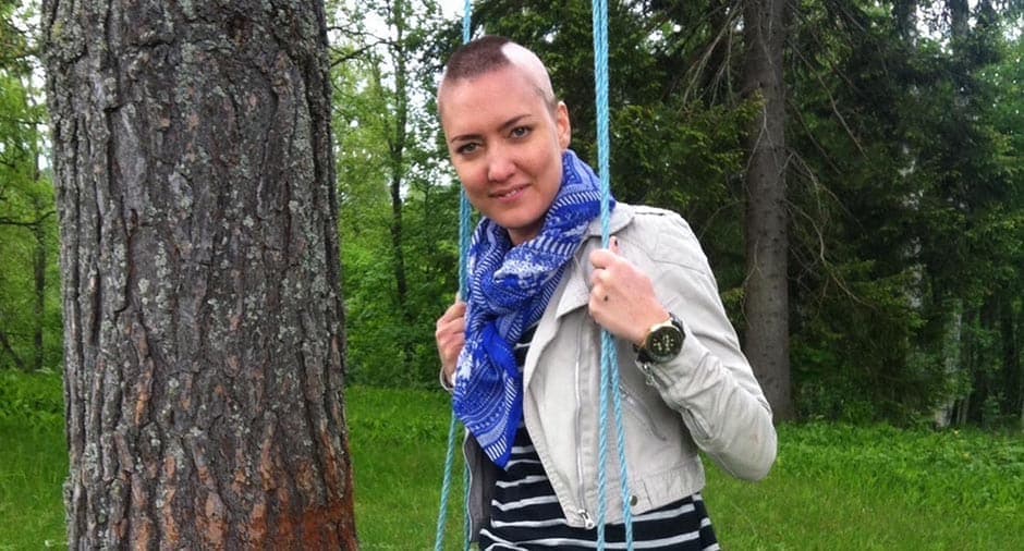 Ung kvinna med snaggat hår sitter på en gunga utomhus i en grönskande miljö.