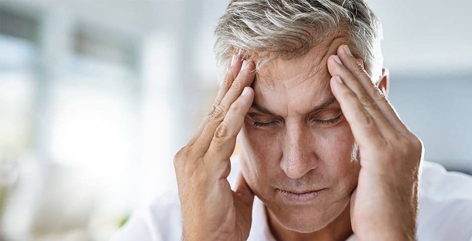 Medelålders man har huvudvärkoch håller sig om huvudetman har svår huvudvärk