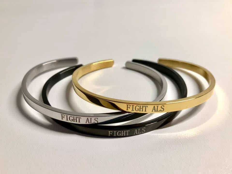 Tre armband i guld, silver och svart med texten "Fight ALS."