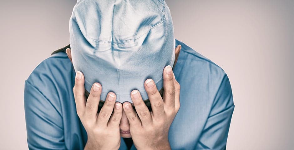 Utmattad sjuksköterska sitter med huvudet i händerna.