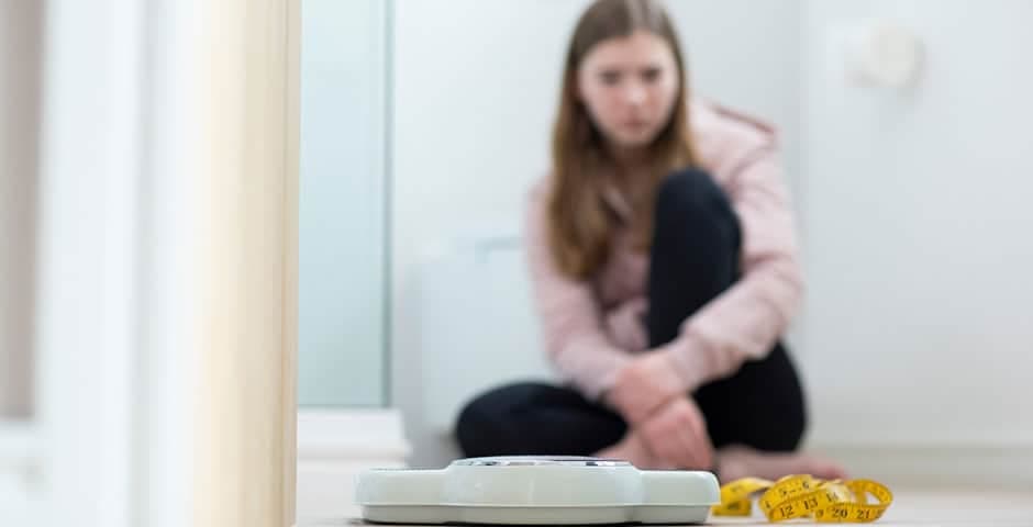 Olycklig tonårsflicka sitter i badrummet och tittar på en våg och måttband
