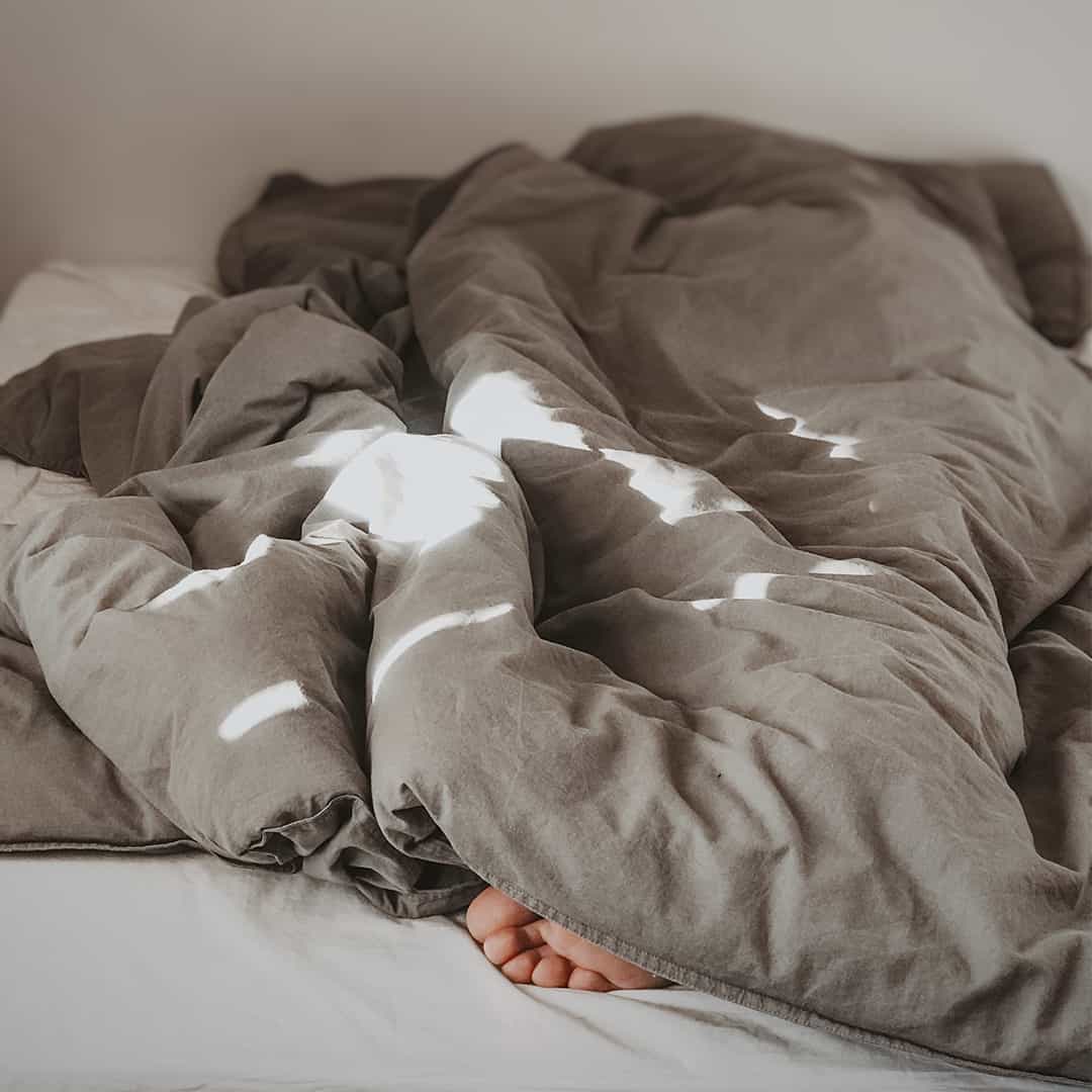 Foto på en säng där man ser en fot stick ut under täcket.