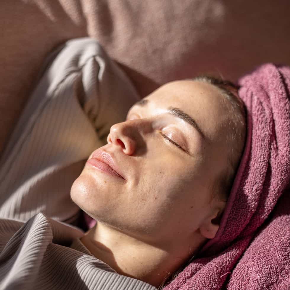 Foto på kvinna som ligger i en soffa med handduk rullad runt håret.