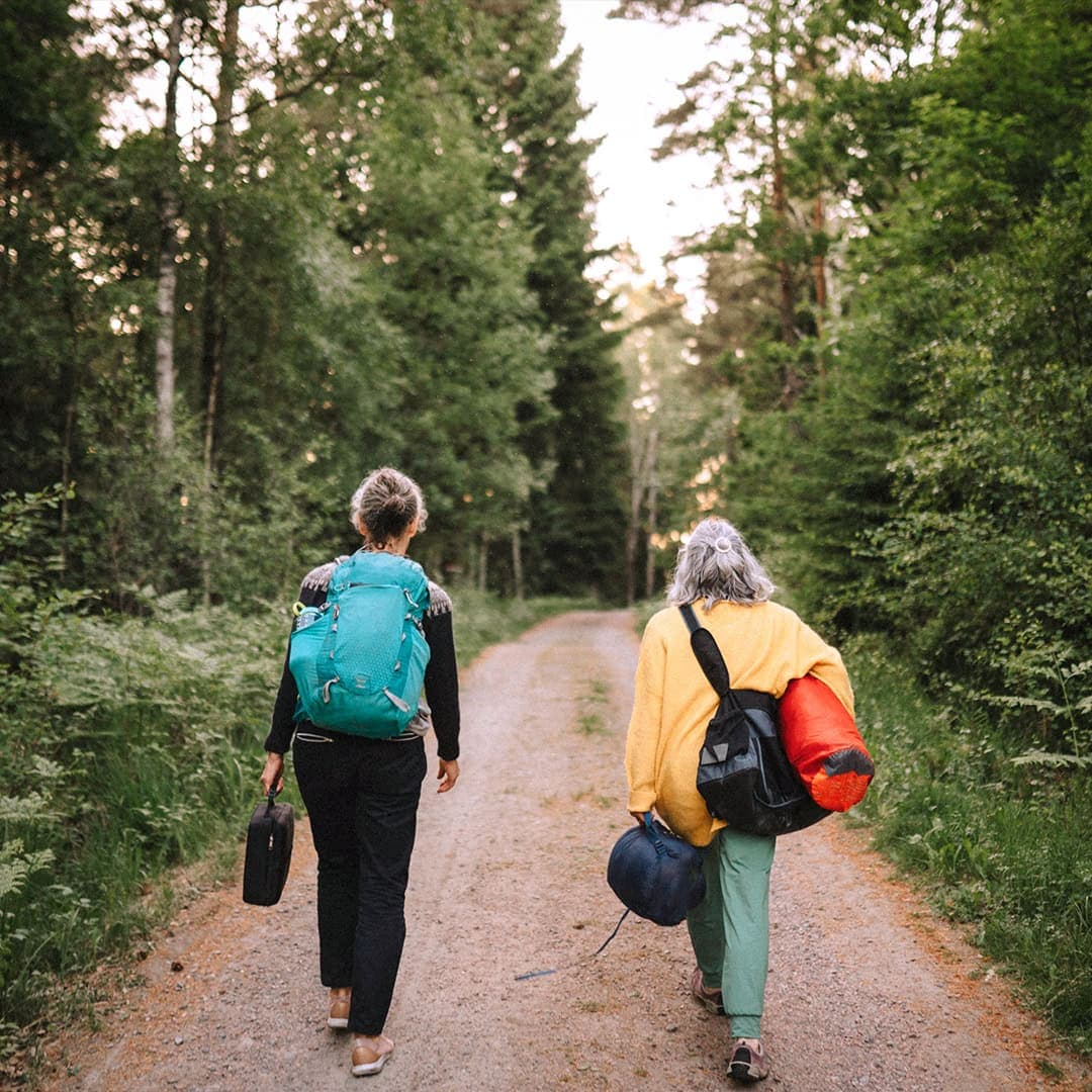 Kvinnliga pensionärer på hajk går i natur med packning.