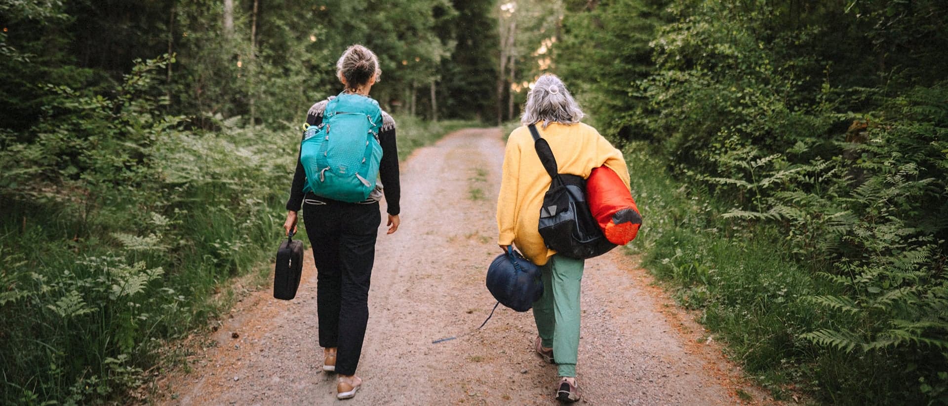 Kvinnliga pensionärer på hajk går i natur med packning.