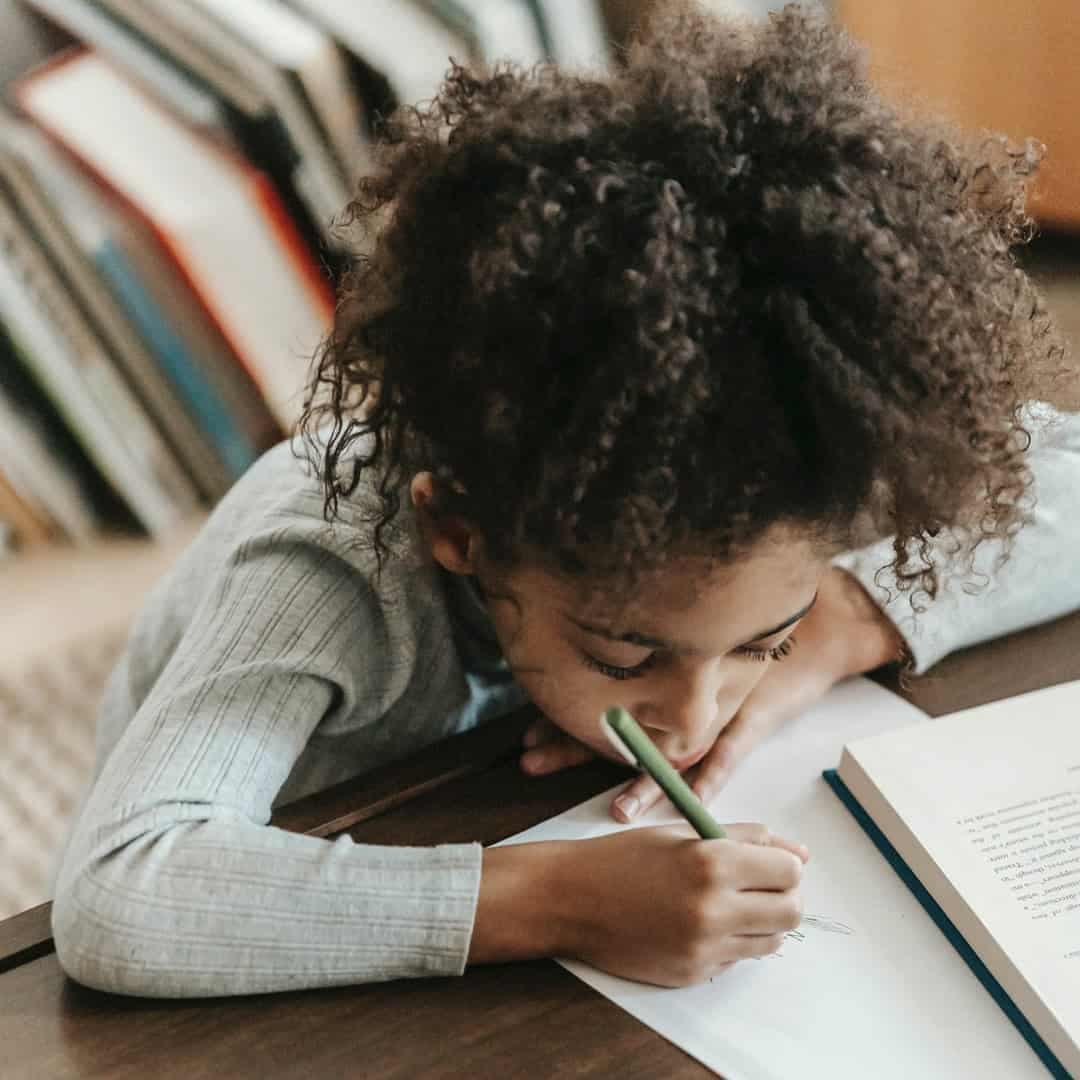 En flicka sitter vid ett bord och skriver på ett papper.