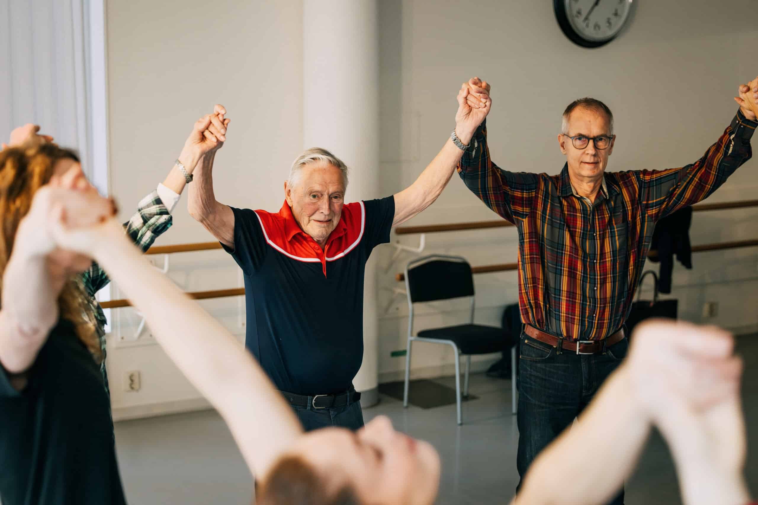 Äldre deltagare håller armarna högt under en gemensam övning i parkinsondans.