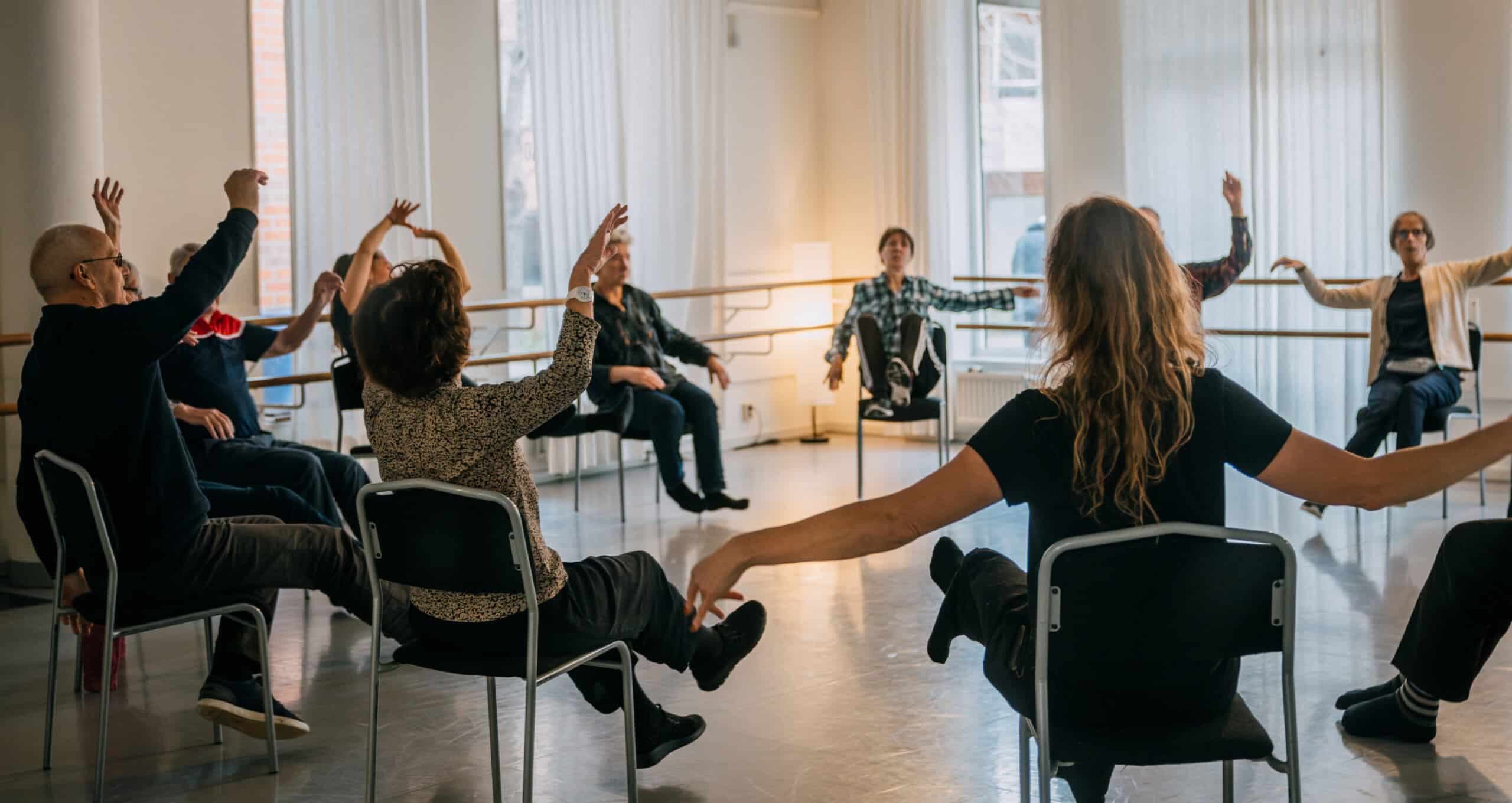 Grupp med personer i olika åldrar sitter på stolar och rör armarna och ben.