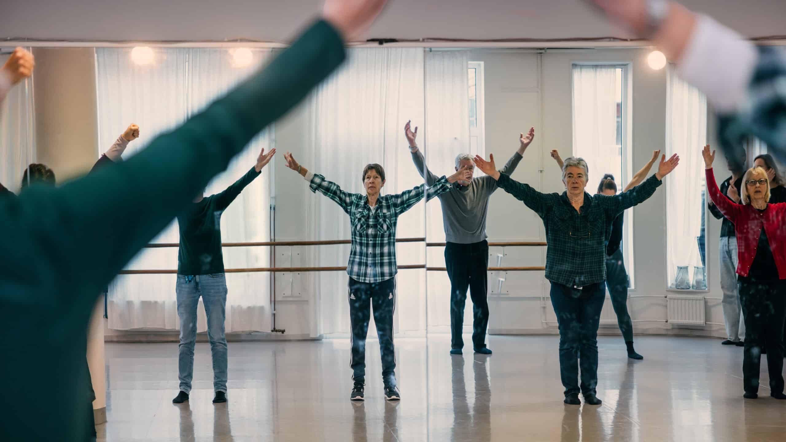 Deltagare står med armarna utsträckta i en dansstudio.