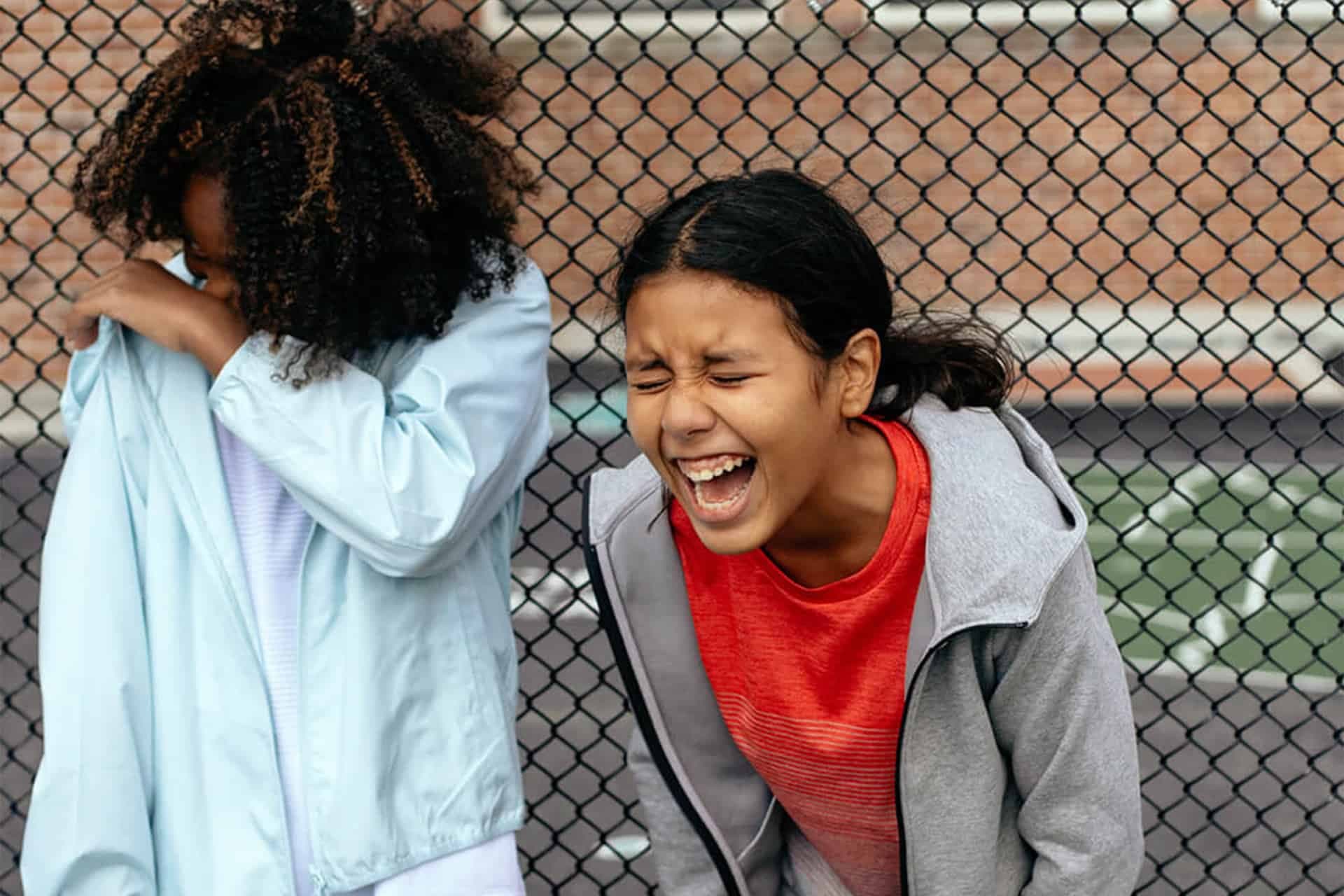 Foto på två tjejer på skolgård som skrattar och leker.