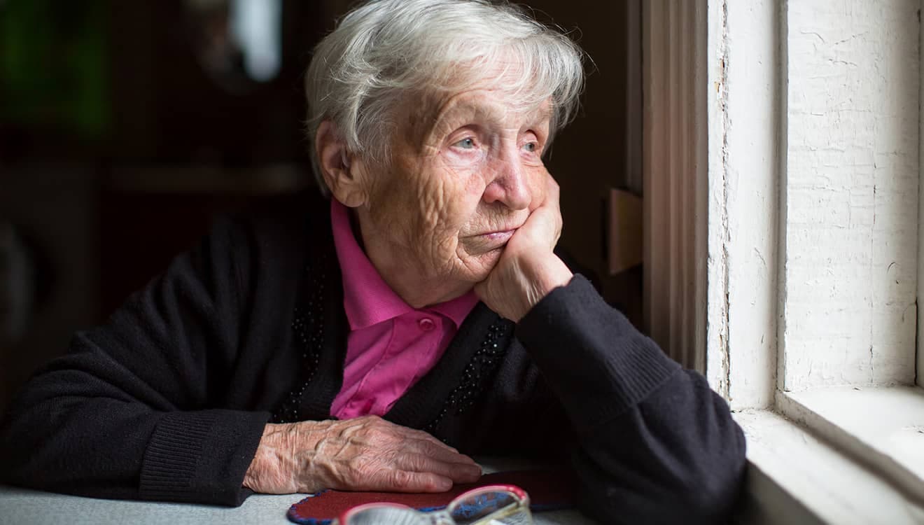 Äldre kvinna tittar sorgset ut genom fönstret