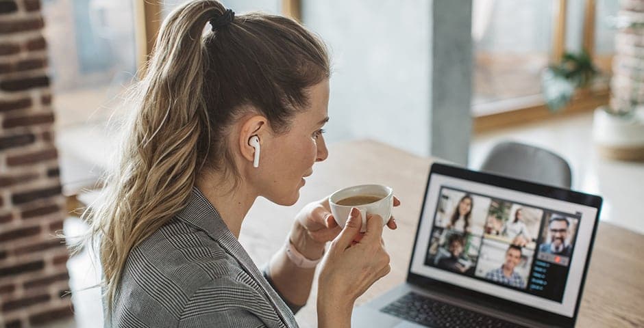 Kvinna sitter med kaffekopp och tittar på ett event på datorn