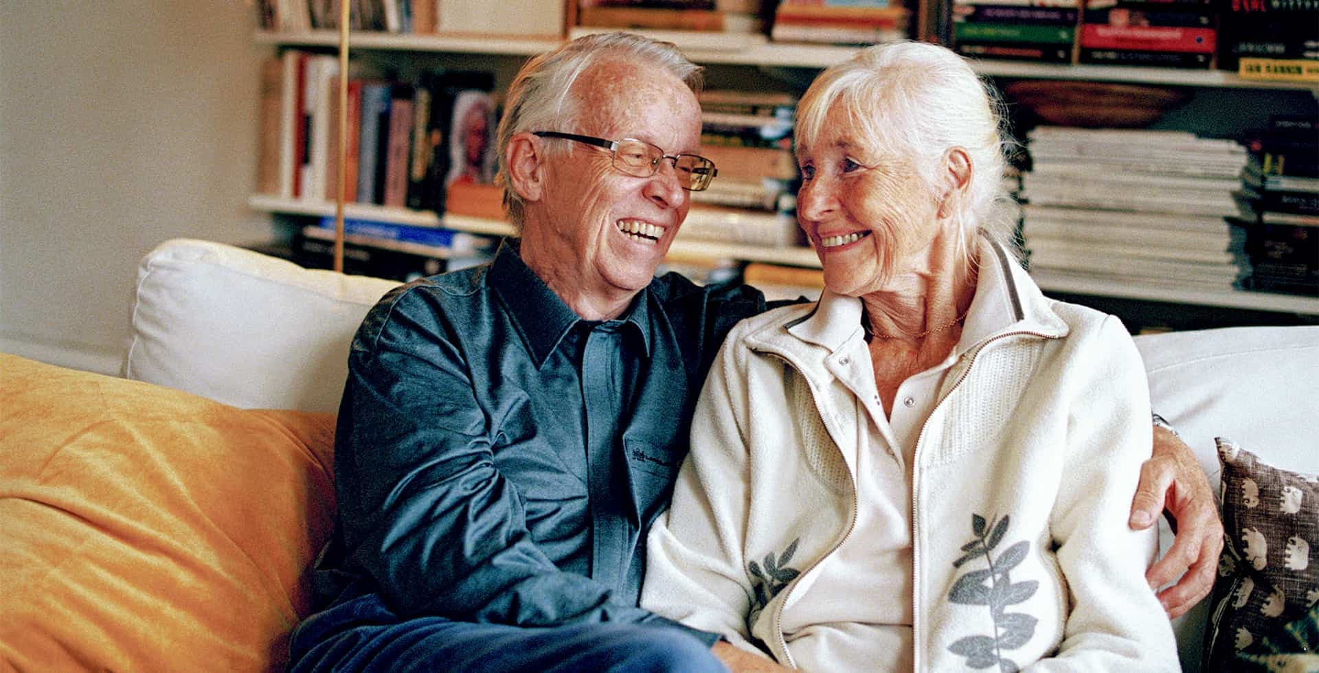 Bild på ett äldre par som sitter i en soffa och tittar på varandra medan de håller om varandra.