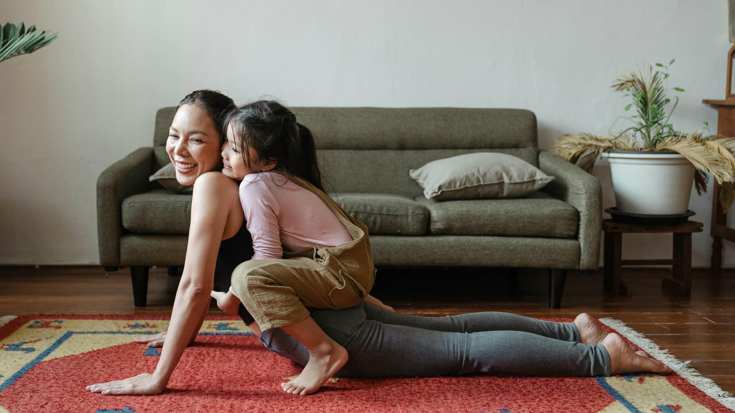 En mamma som yogar hemma och hennes dotter som klättrar på henne.