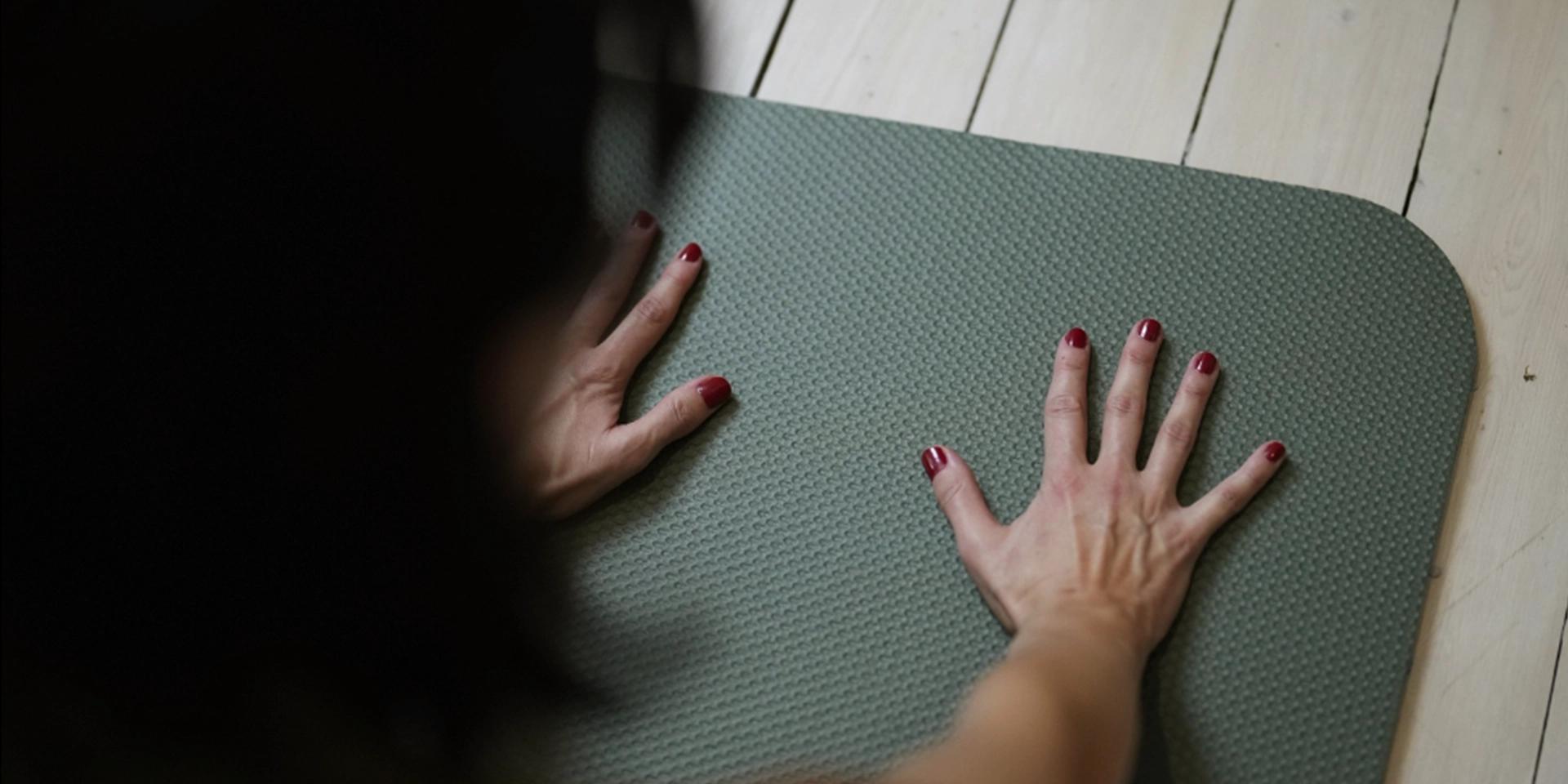 Bild händer i en yogamatta. Tagen över axlen på person som gör yoga.