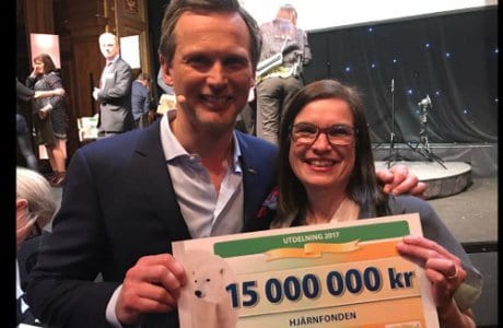 Porträtt av Rickard Sjöberg från Postkodlotteriet och Anna Hemlin som håller i en check på 15 miljoner kronor.