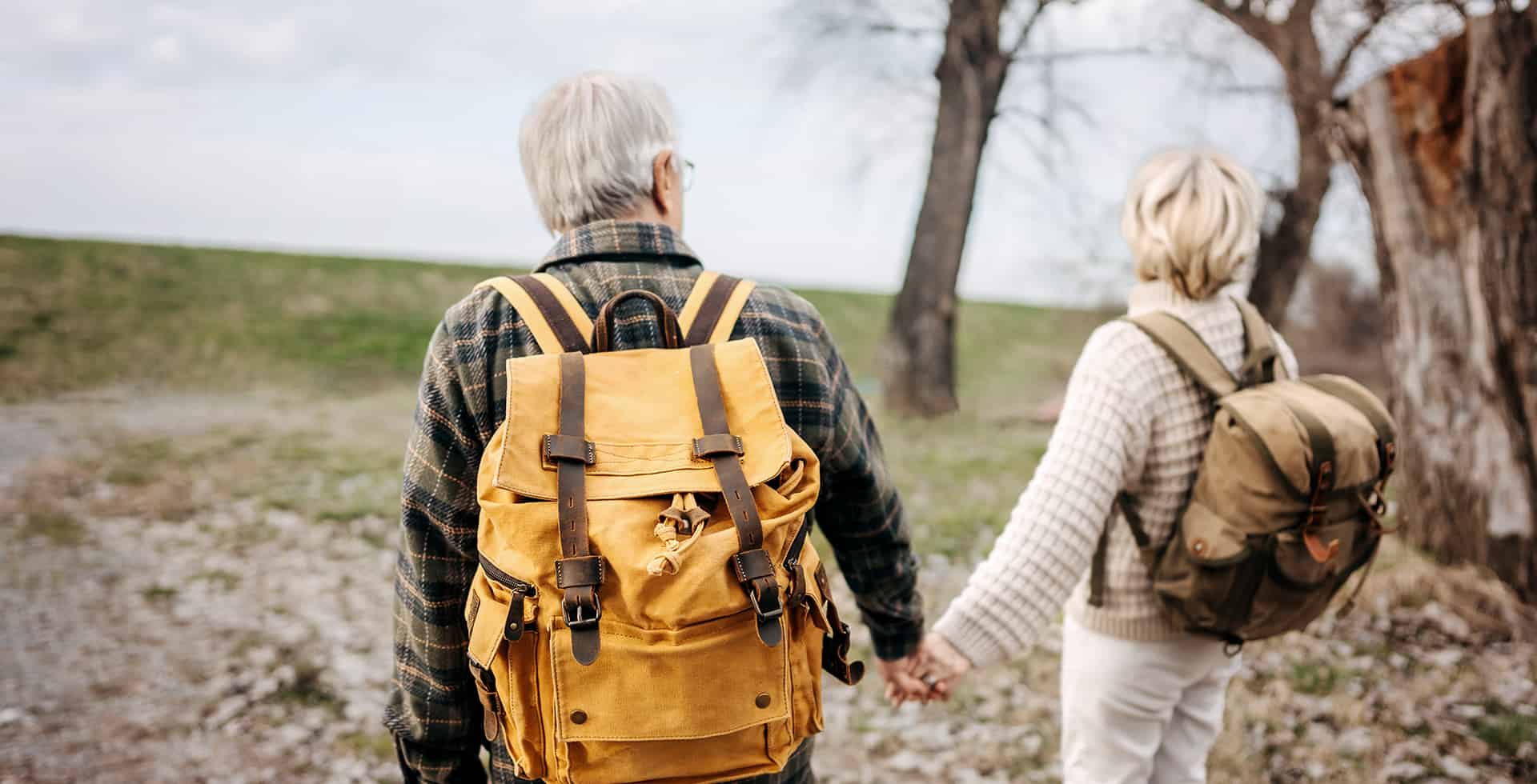 Två äldre gråhåriga personer håller handen ute i naturen.