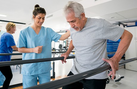 En man håller sig i två räcken och tränar på att gå.