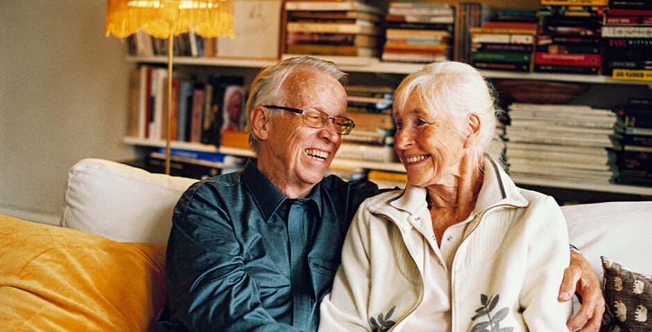 Ett leende äldre par sitter ien soffa och håller om varandra
