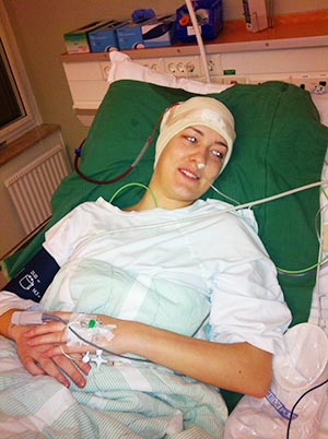 Ung kvinna i sjukhussäng med bandage runt huvudet. 
