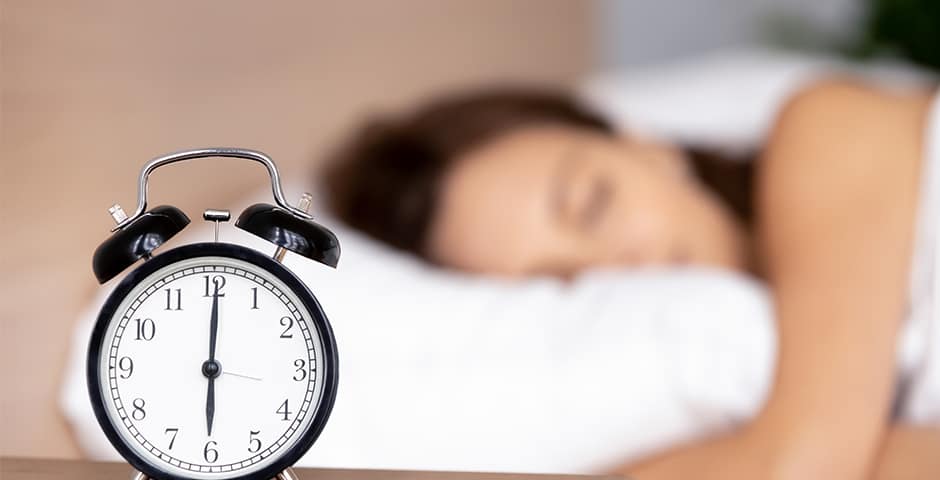 Kvinna sover och på nattduksbordet står en väckarklocka