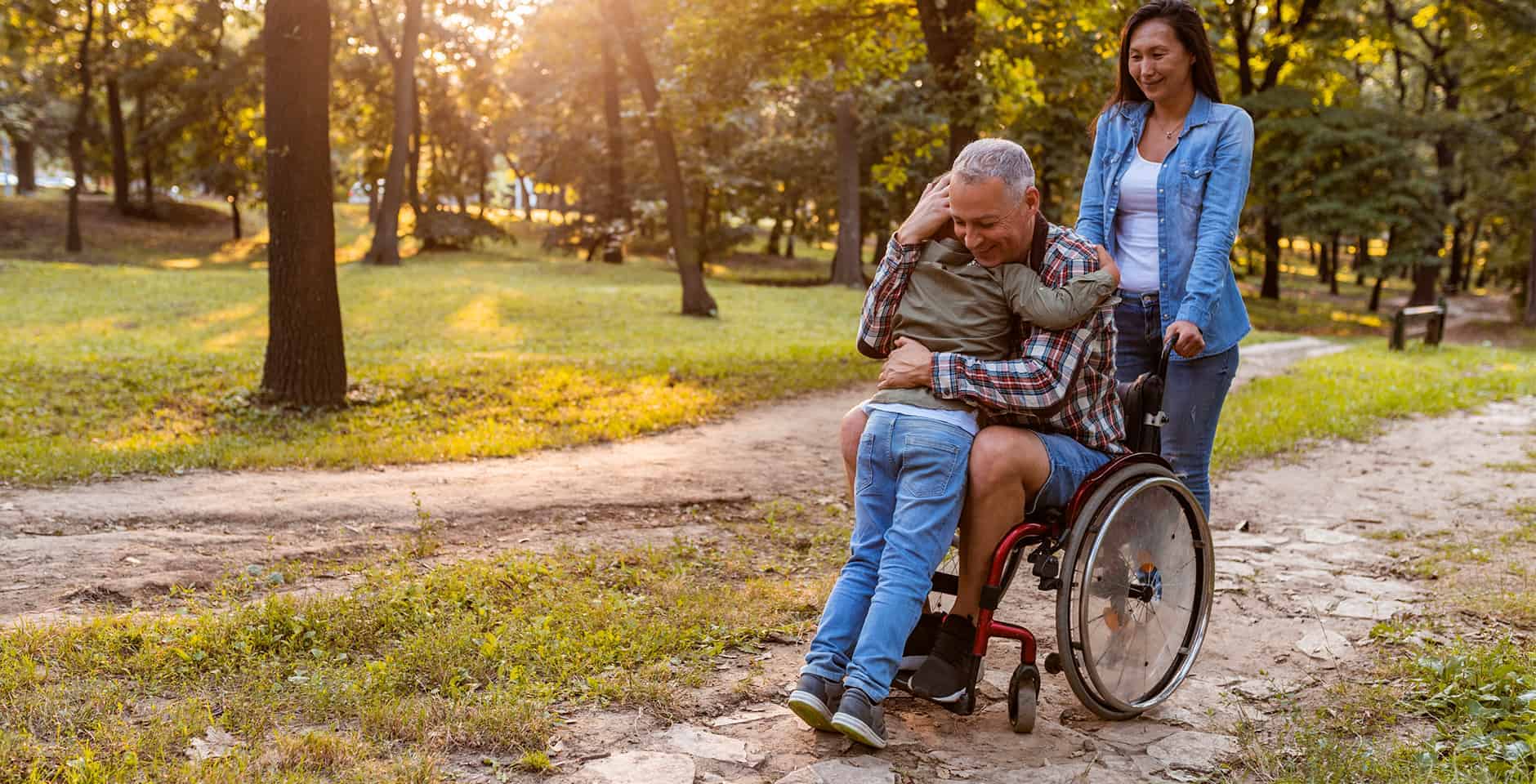 Äldre man sitter i rullstol och kramar om sitt barnbarn