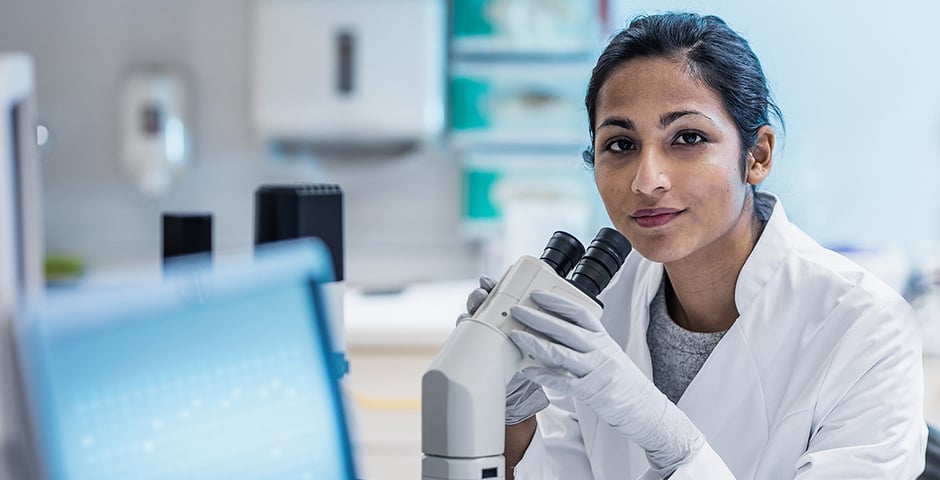 Kvinnlig forskare sitter vid mikroskop