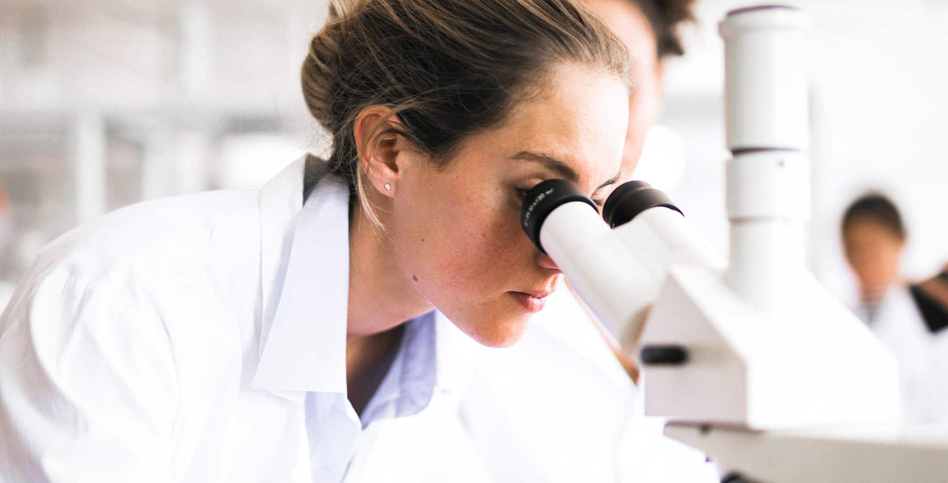 En ung kvinna i ett labb som tittar i ett mikroskop
